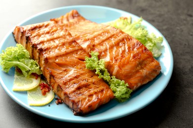 Photo of Delicious grilled salmon fillets with lettuce and lemon on grey table, closeup