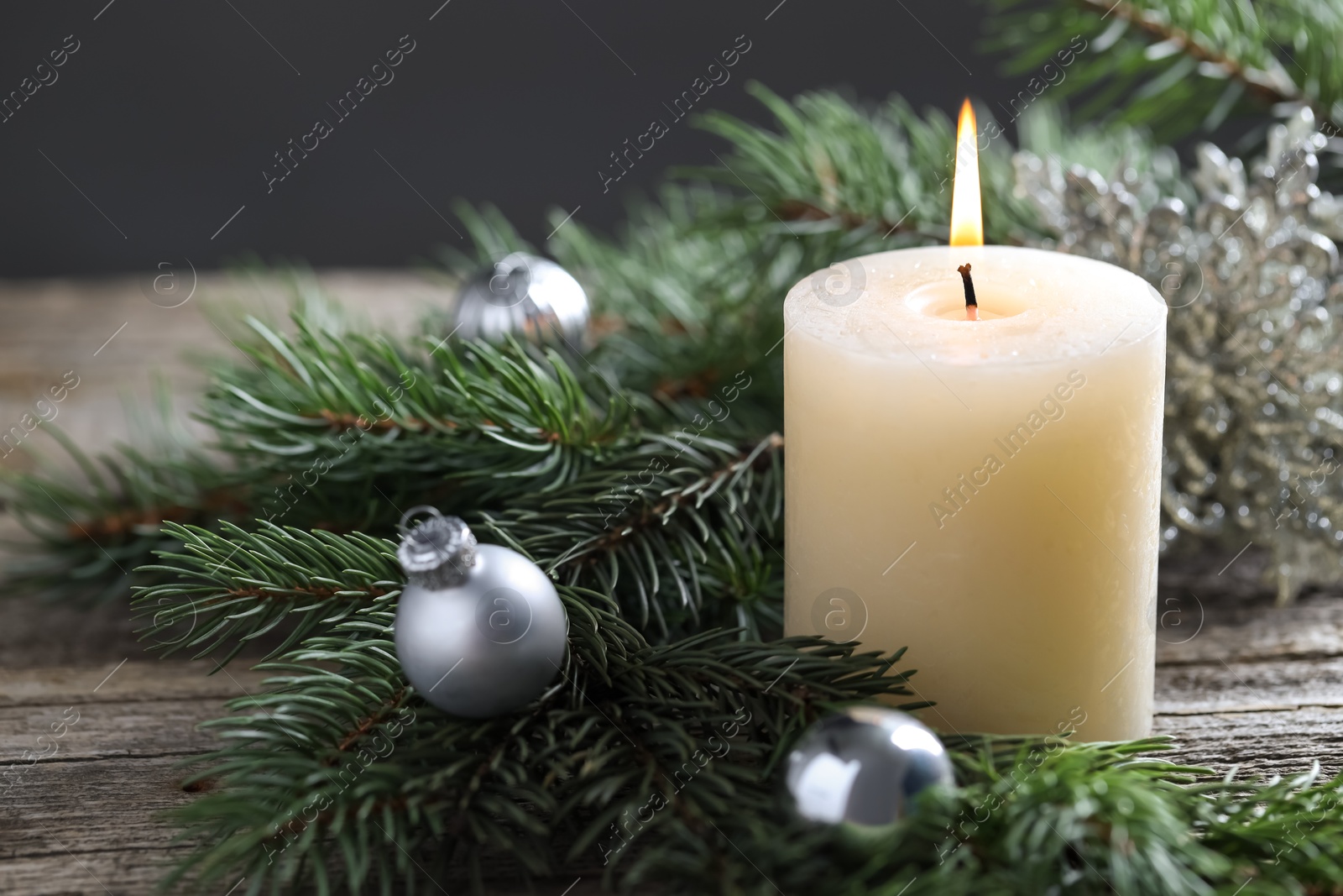 Photo of Burning candle, baubles and fir tree branches on wooden table, closeup