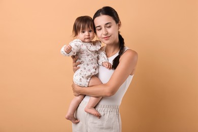 Beautiful young mother and her cute little baby on beige background