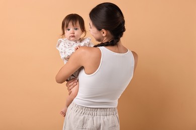 Beautiful young mother and her cute little baby on beige background