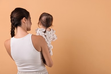 Photo of Beautiful young mother and her cute little baby on beige background, back view. Space for text