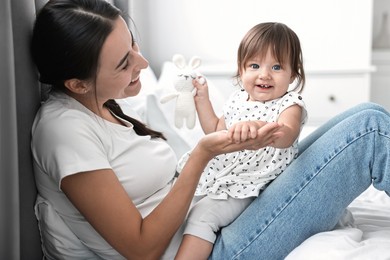 Beautiful young mother and her cute little baby with rabbit toy on bed at home