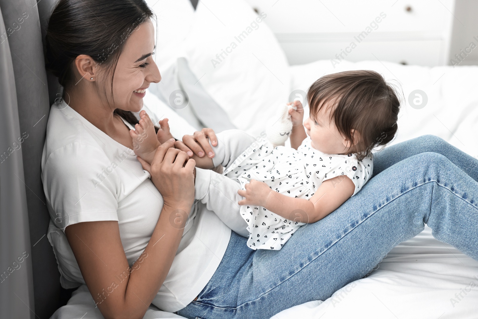 Photo of Beautiful young mother and her cute little baby with rabbit toy on bed at home