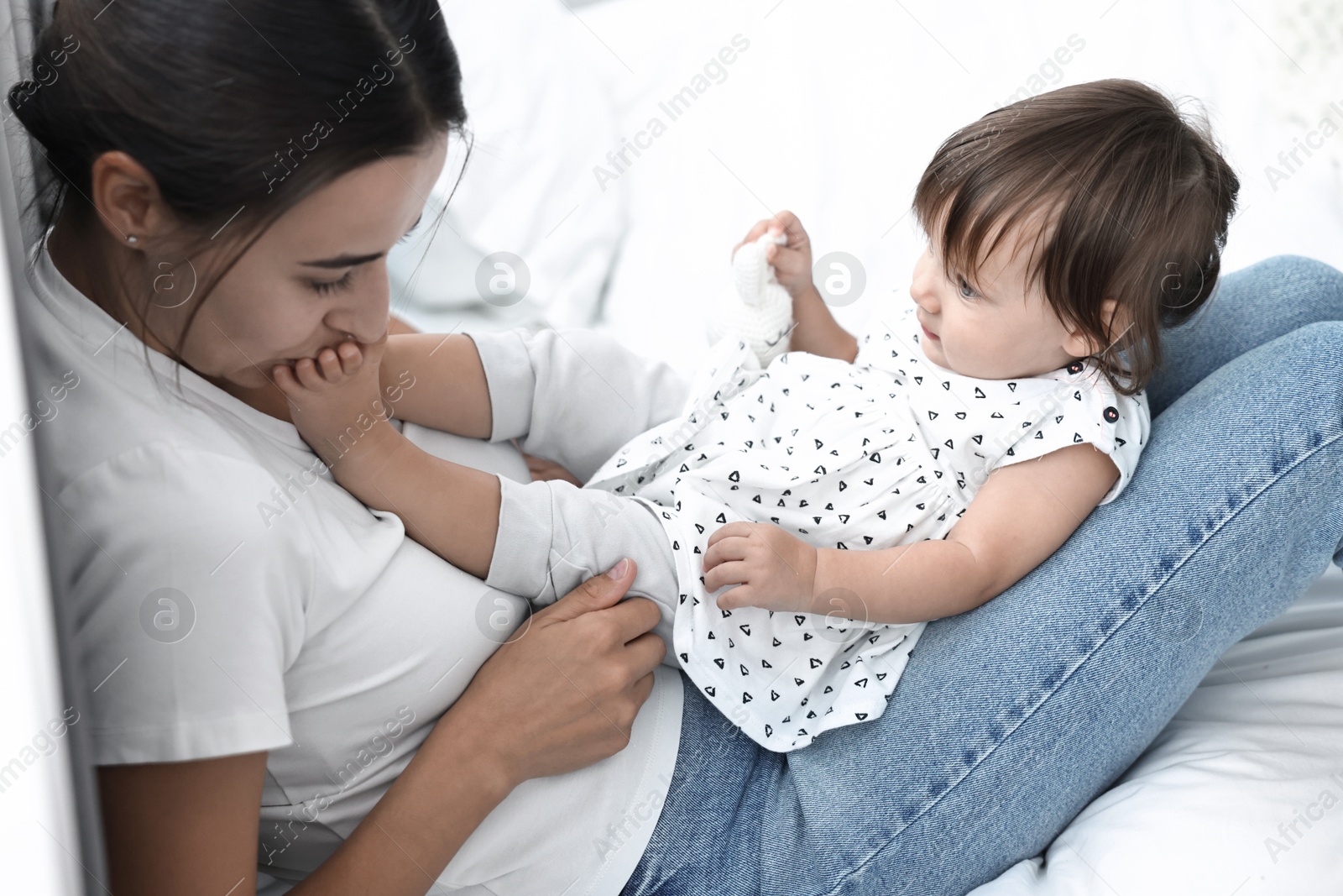 Photo of Beautiful young mother and her cute little baby with rabbit toy on bed at home