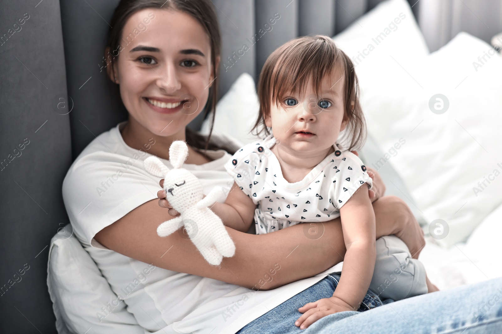 Photo of Beautiful young mother and her cute little baby with rabbit toy on bed at home