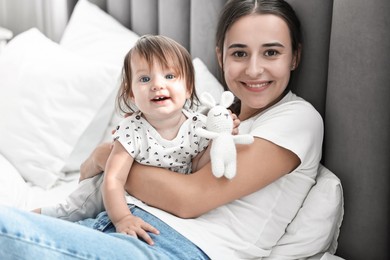 Beautiful young mother and her cute little baby with rabbit toy on bed at home