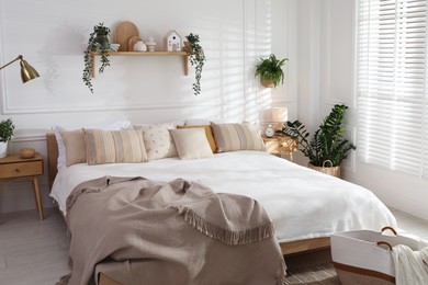 Photo of Stylish bedroom interior with large bed, houseplants and decorative elements