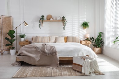 Photo of Stylish bedroom interior with large bed, houseplants and decorative elements