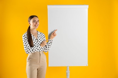 Photo of Happy woman near flip chart on orange background. Mockup for design