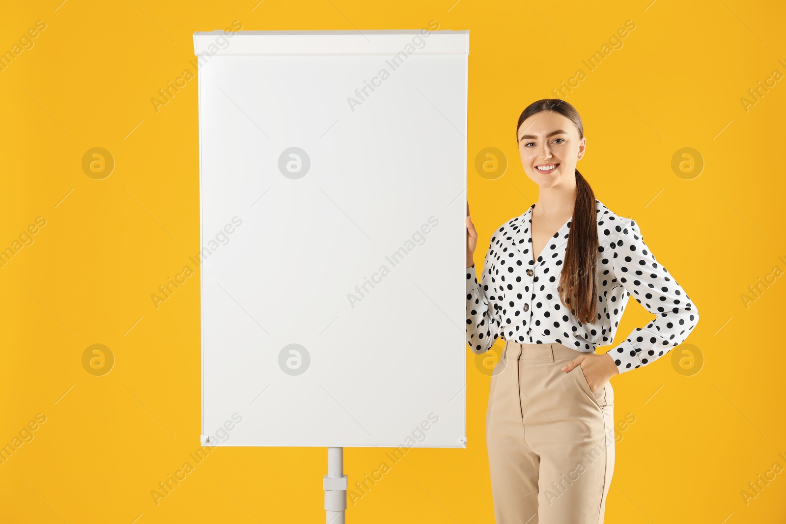 Photo of Happy woman near flip chart on orange background. Mockup for design