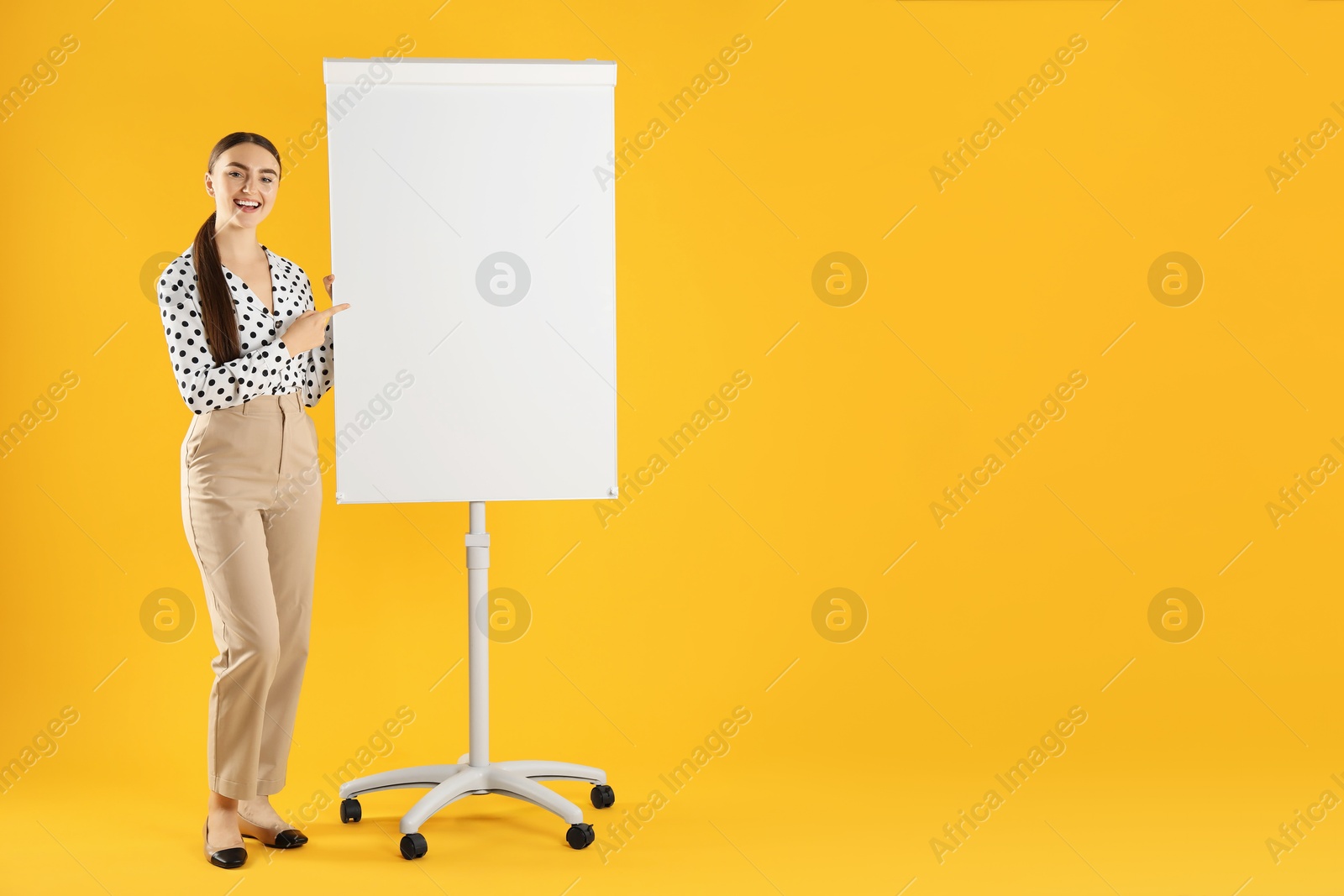 Photo of Happy woman near flip chart on orange background. Mockup for design