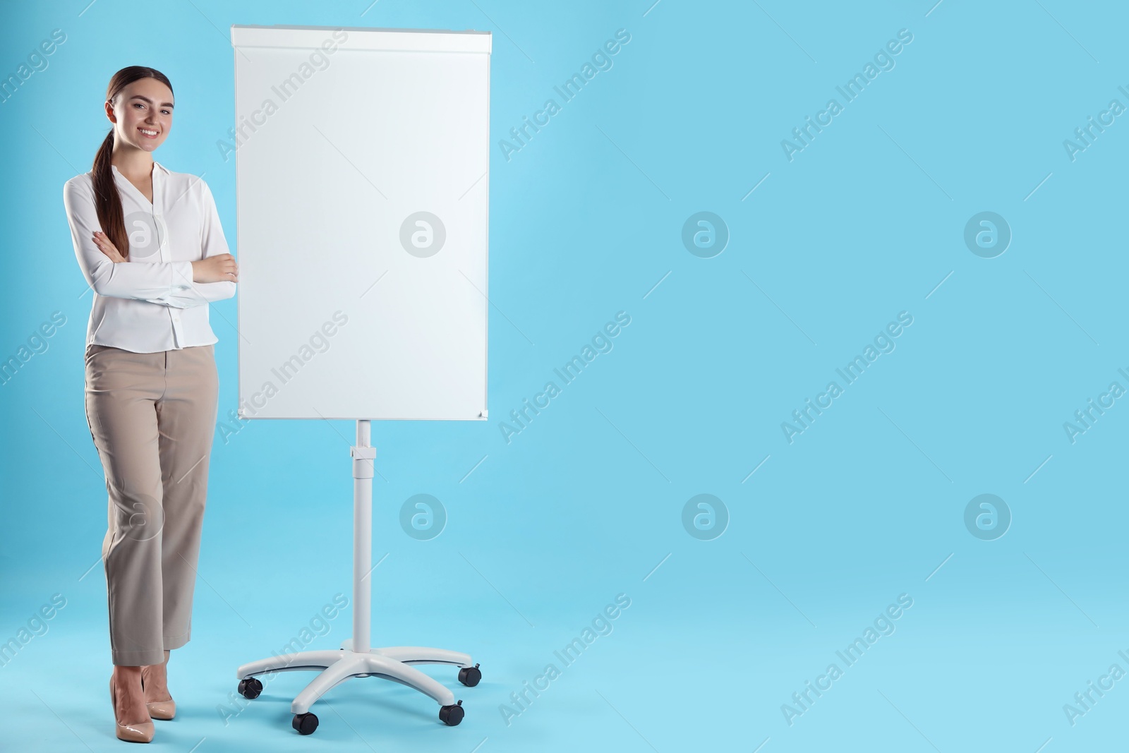 Photo of Happy woman near flip chart on light blue background. Mockup for design