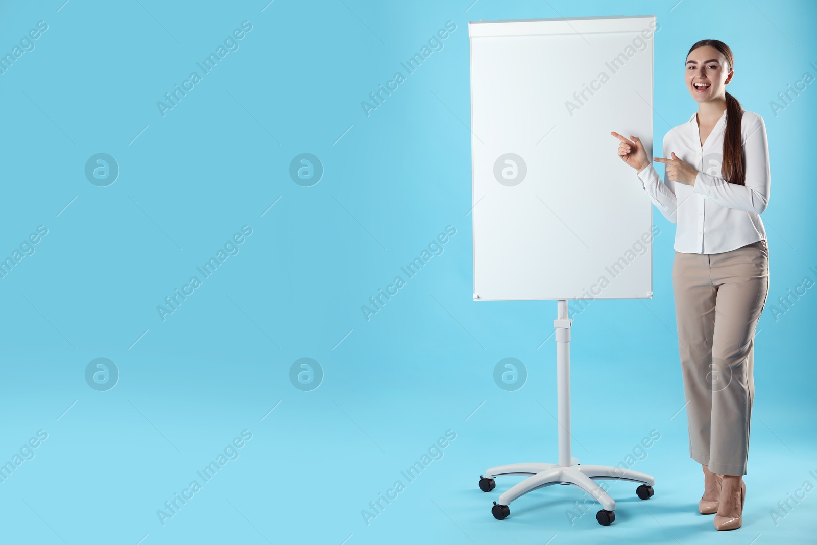 Photo of Happy woman near flip chart on light blue background. Mockup for design