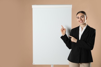 Happy woman near flip chart on pale brown background. Mockup for design