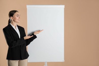 Photo of Happy woman near flip chart on pale brown background. Mockup for design