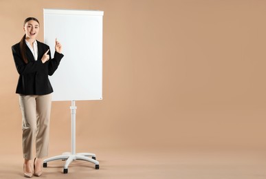 Happy woman near flip chart on pale brown background. Mockup for design