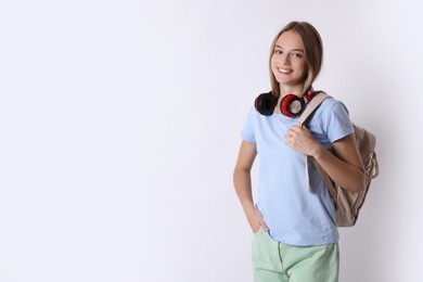 Teenage girl with headphones and backpack on white background, space for text