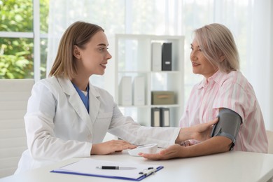 Doctor measuring patient's blood pressure at table in hospital