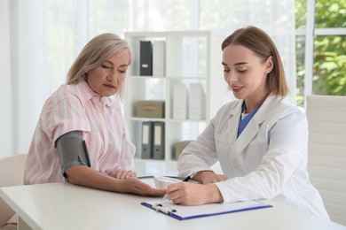 Doctor measuring patient's blood pressure at table in hospital