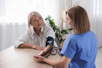 Healthcare worker measuring patient's blood pressure at wooden table indoors