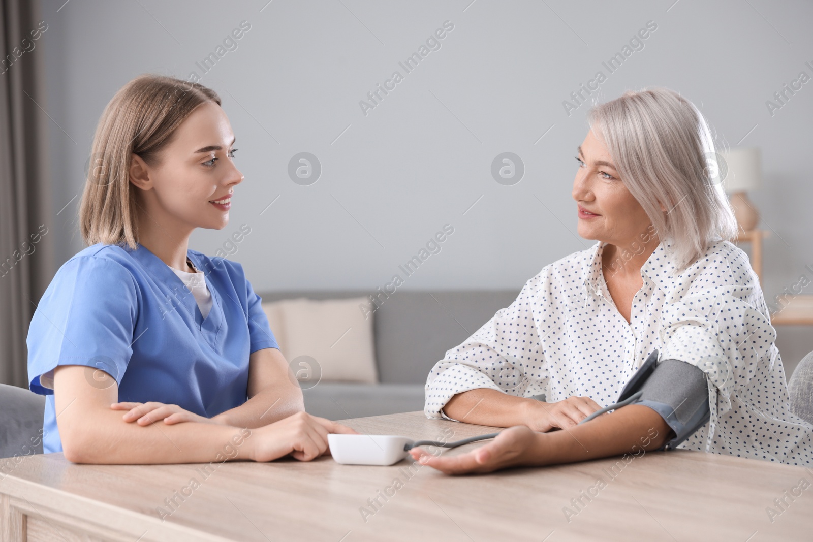 Photo of Healthcare worker measuring patient's blood pressure at wooden table indoors