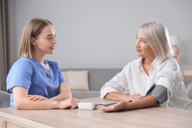 Healthcare worker measuring patient's blood pressure at wooden table indoors