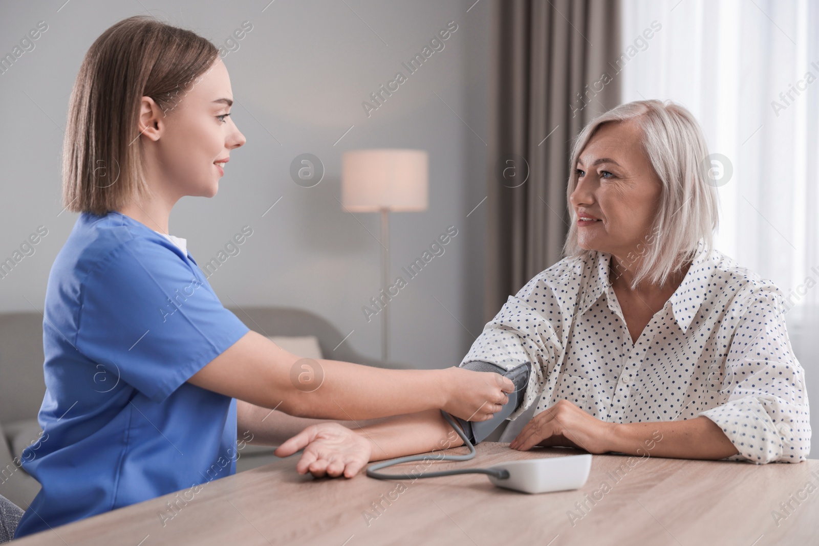 Photo of Healthcare worker measuring patient's blood pressure at wooden table indoors