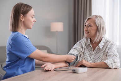 Photo of Healthcare worker measuring patient's blood pressure at wooden table indoors