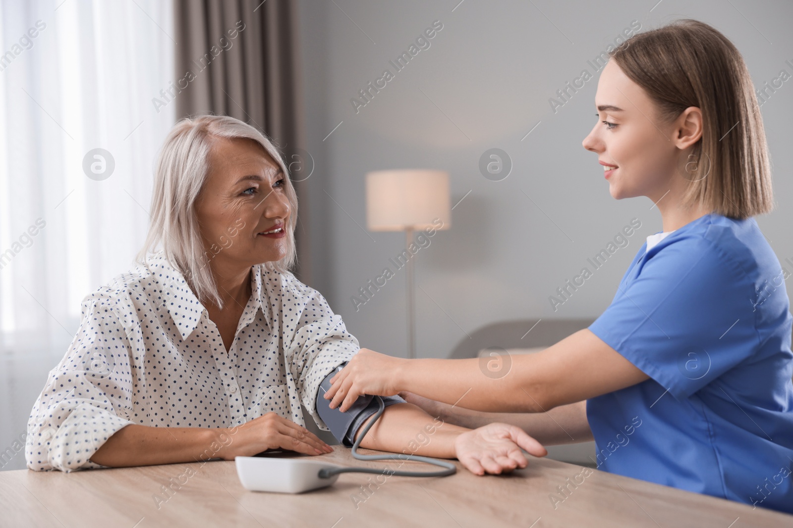 Photo of Healthcare worker measuring patient's blood pressure at wooden table indoors