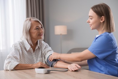 Photo of Healthcare worker measuring patient's blood pressure at wooden table indoors