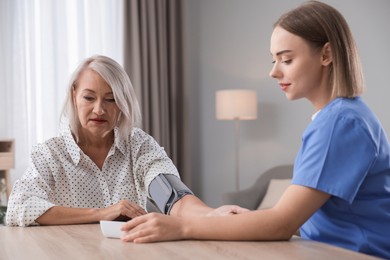 Photo of Healthcare worker measuring patient's blood pressure at wooden table indoors