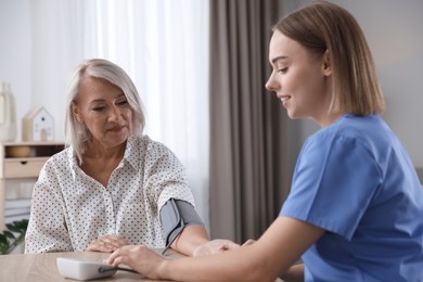 Photo of Healthcare worker measuring patient's blood pressure at wooden table indoors