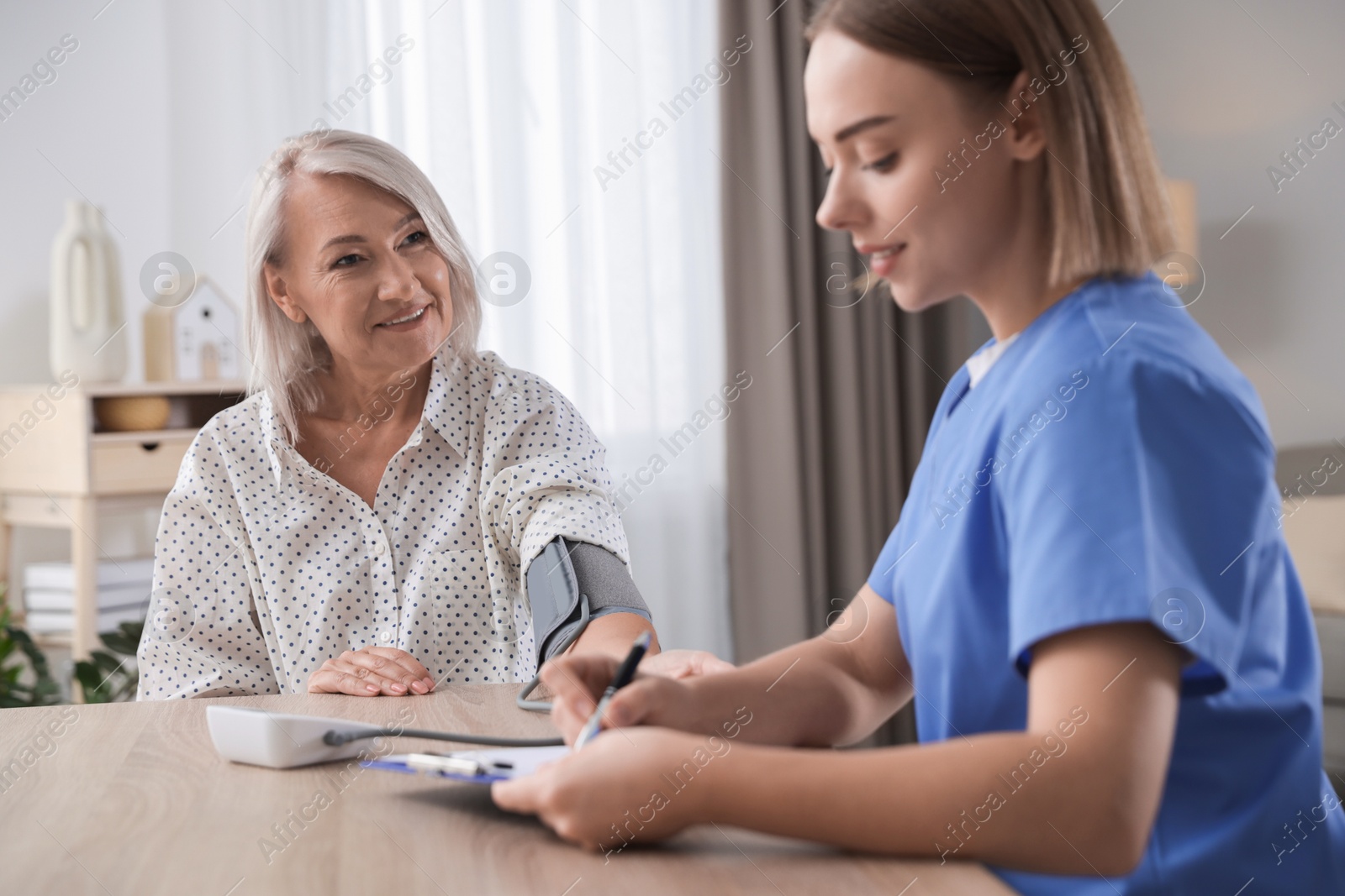 Photo of Healthcare worker measuring patient's blood pressure at wooden table indoors