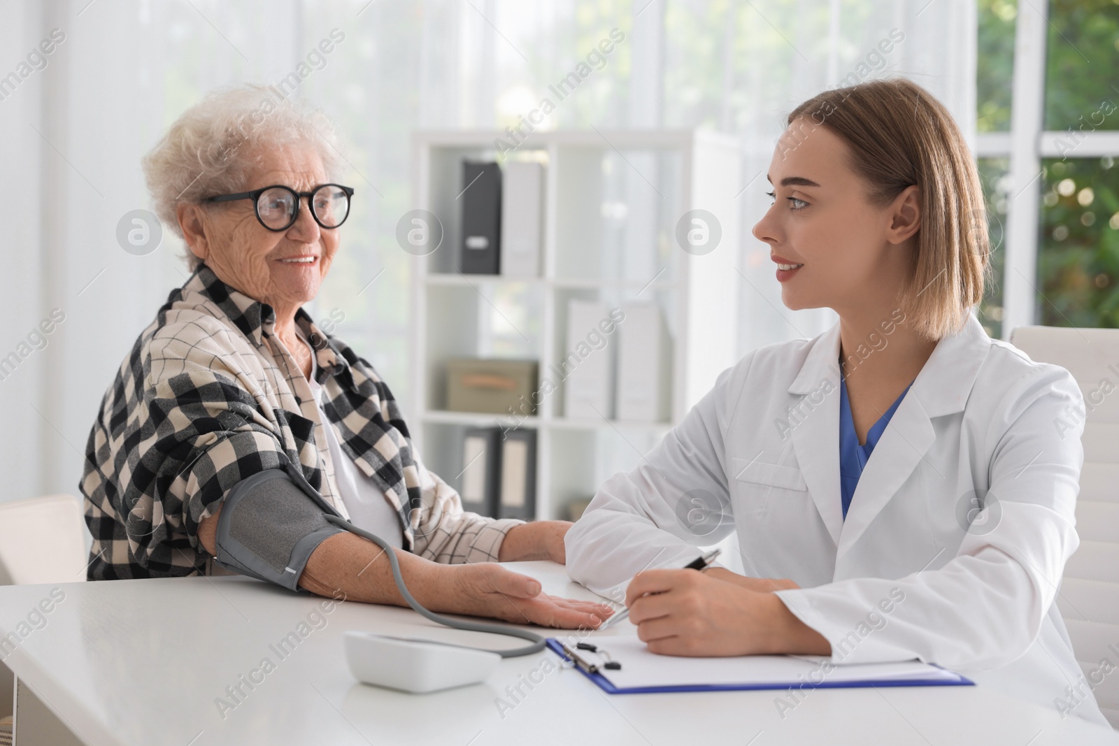 Photo of Doctor measuring patient's blood pressure at table in hospital