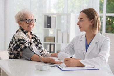 Doctor measuring patient's blood pressure at table in hospital