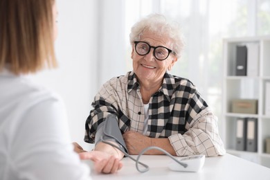 Doctor measuring patient's blood pressure at table in hospital