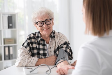 Doctor measuring patient's blood pressure at table in hospital