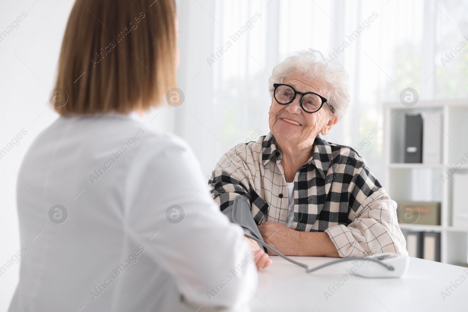 Photo of Doctor measuring patient's blood pressure at table in hospital