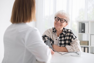 Photo of Doctor measuring patient's blood pressure at table in hospital