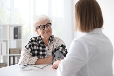 Doctor measuring patient's blood pressure at table in hospital