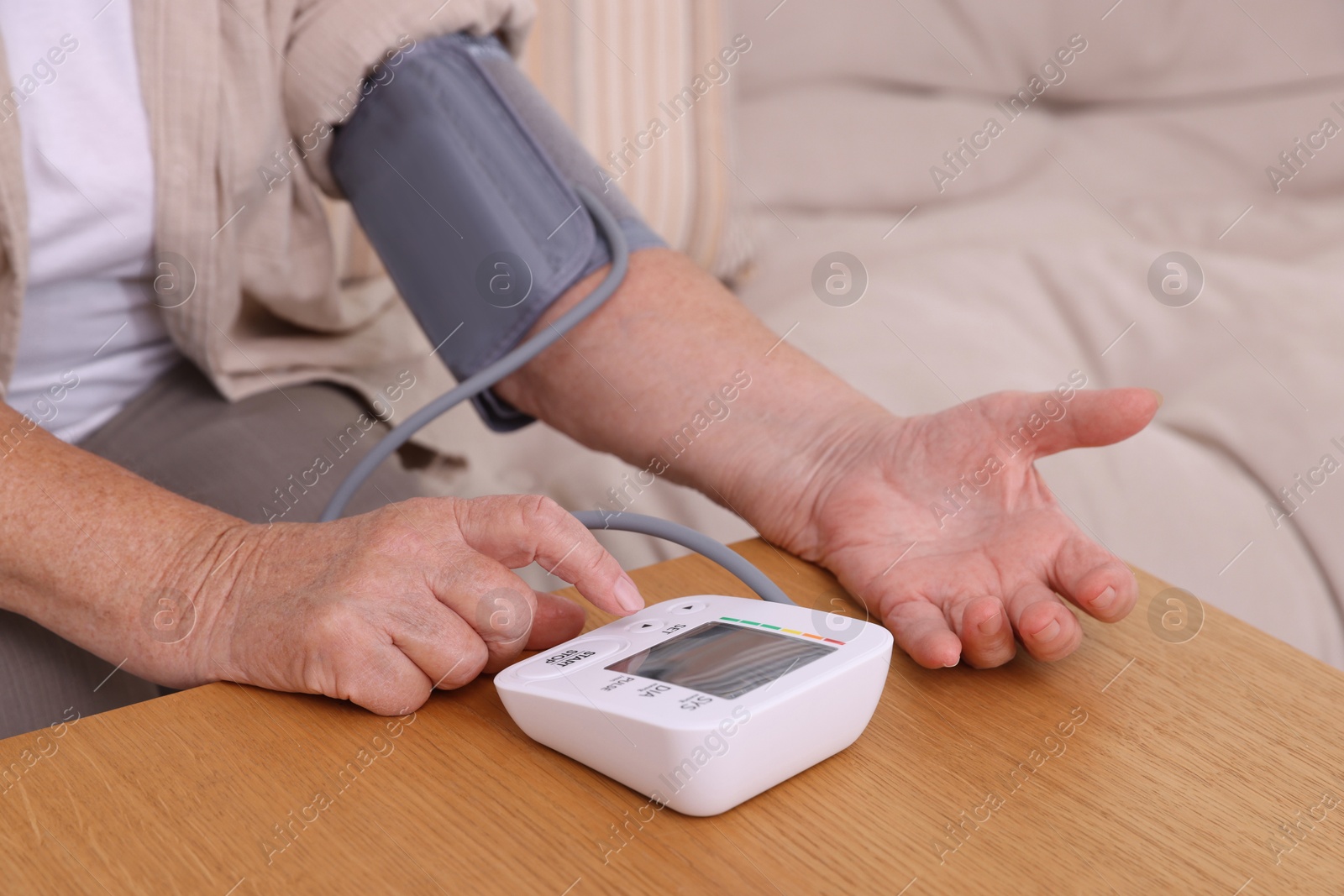 Photo of Senior woman measuring blood pressure at wooden table indoors, closeup