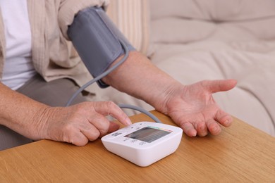 Photo of Senior woman measuring blood pressure at wooden table indoors, closeup