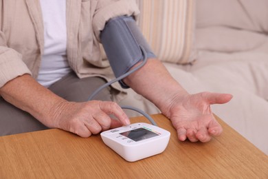 Senior woman measuring blood pressure at wooden table indoors, closeup