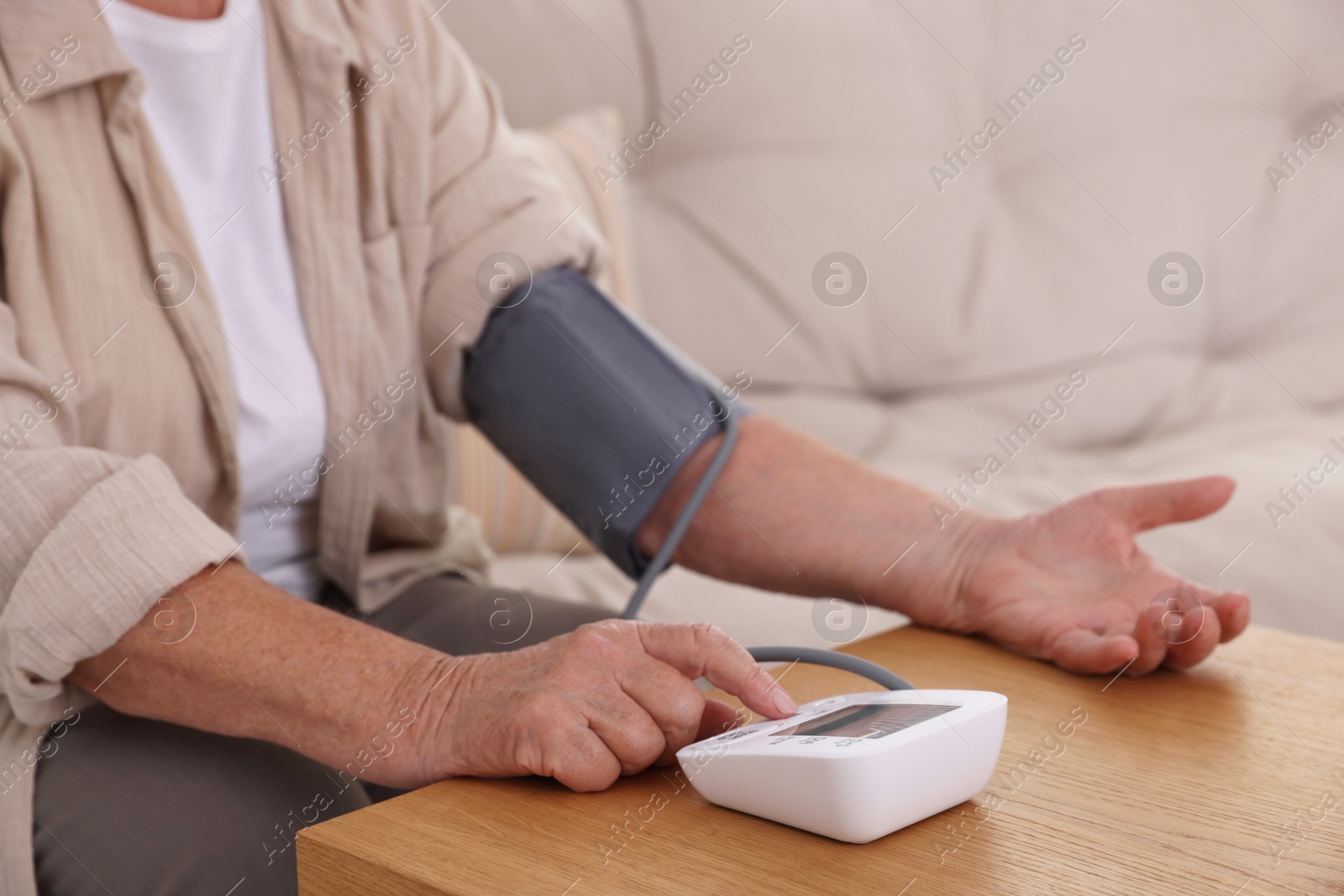 Photo of Senior woman measuring blood pressure at wooden table indoors, closeup