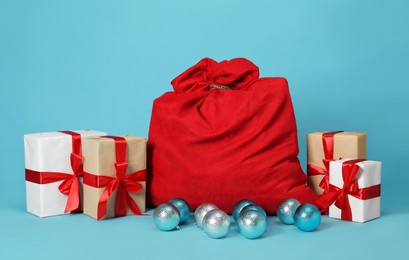 Photo of Santa Claus bag with baubles and gift boxes on light blue background