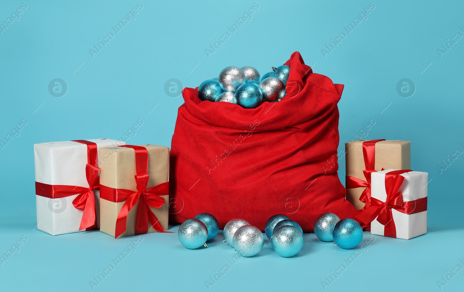 Photo of Santa Claus bag with baubles and gift boxes on light blue background