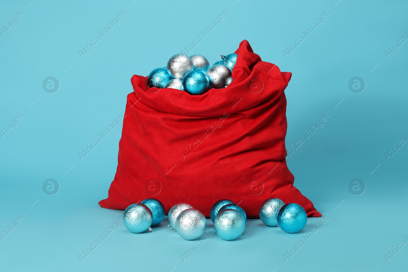 Photo of Santa Claus bag with baubles on light blue background