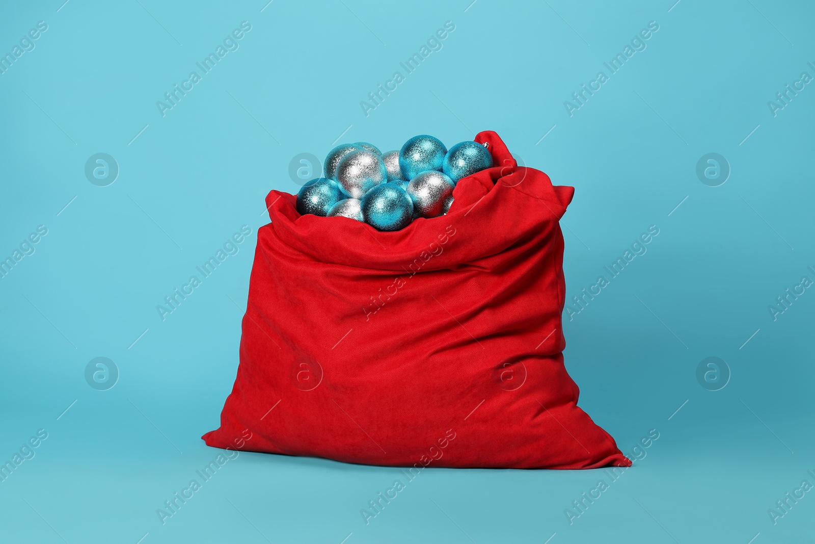 Photo of Santa Claus bag with baubles on light blue background