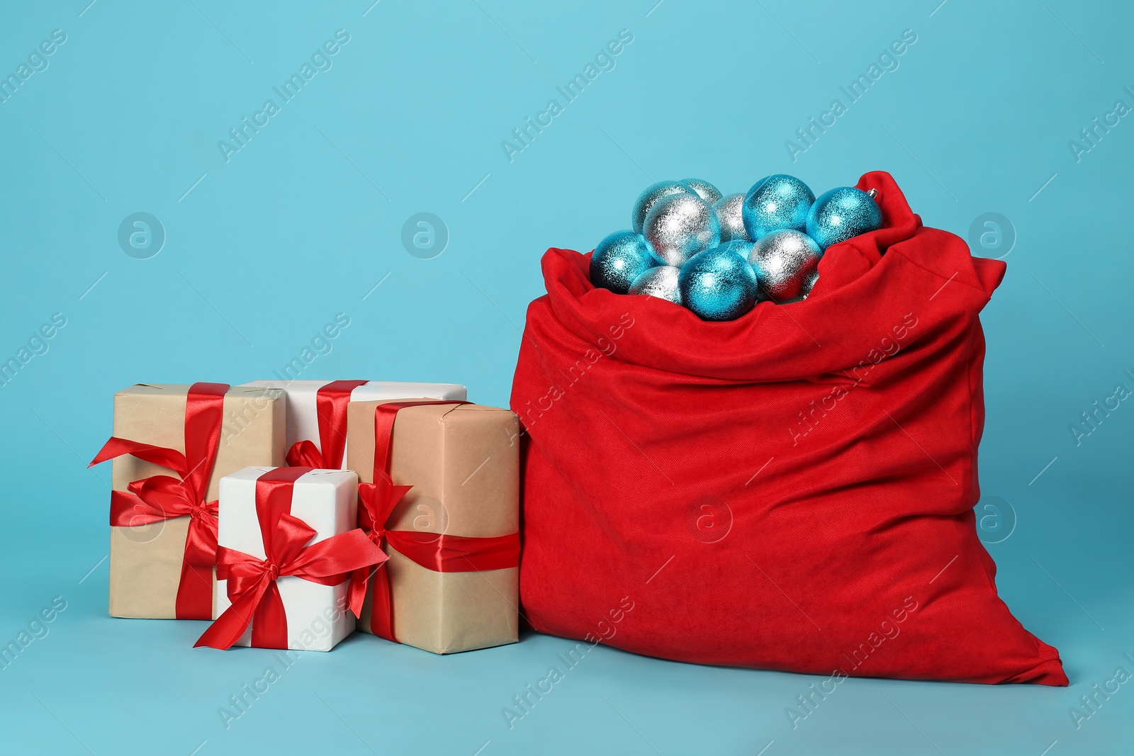 Photo of Santa Claus bag with baubles and gift boxes on light blue background