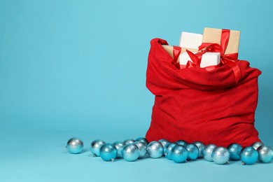 Photo of Santa Claus bag with baubles and gift boxes on light blue background, space for text